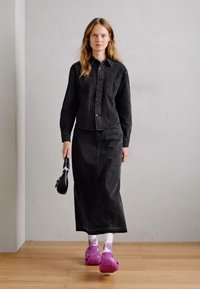 Chemise noire en denim à boutons avec un motif texturé, associée à une jupe longue noire. Comprend des sabots violets éclatants et des chaussettes blanches avec des motifs violets.