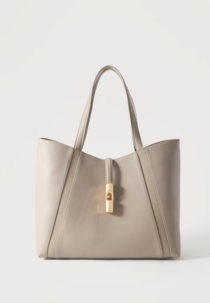 Beige lædertaske med to håndtag og en central guldlås detalje, stående opret på en hvid baggrund.