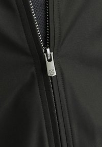 Detalles de una chaqueta negra con un cierre plateado, textura textil y un logo en el tirador del zipper, resaltando elementos de diseño elegantes.