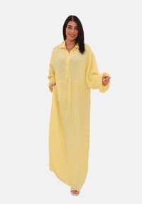 Abito maxi giallo a maniche lunghe realizzato in tessuto leggero e testurizzato, con una chiusura a bottoni sul davanti e maniche oversize.