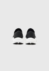 Baskets en tricot noires avec une tige texturée et une semelle en caoutchouc blanche, présentant un profil bas et un design de talon arrondi.