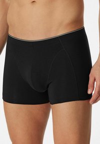 Black cotton boxer shorts with a fitted design, featuring a contrasting waistband and stitching details. Smooth texture and mid-thigh length.