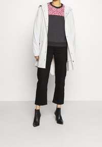 Impermeable gris claro con capucha sobre sudadera gris oscuro que presenta un yoké de diseño rojo, combinado con pantalones negros recortados y botines negros de tacón.