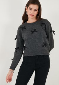 Grijs gebreid sweater met zwarte strikaccenten, ronde hals, lange mouwen en een geribbelde zoom. Zachte textuur en een relaxte pasvorm.