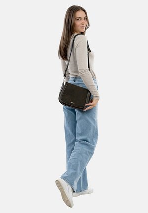 Black leather crossbody bag with a curved shape, silver hardware, and decorative stitching. Model wears a beige top and light blue jeans.