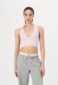 Svijetlo ružičasti rebrasti crop top s dubokim V-dekolteom, minimalnog dizajna, uparen s sivim trenirkama koje imaju elastičnu struk i vezicu.