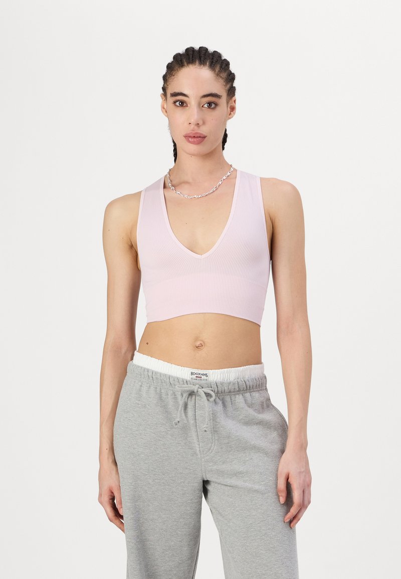 Svijetlo ružičasti rebrasti crop top s dubokim V-dekolteom, minimalnog dizajna, uparen s sivim trenirkama koje imaju elastičnu struk i vezicu.