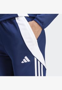 Marineblaue Sporthosen mit weißen Seitenstreifen und kleinem weißen Adidas-Logo. Verfügt über eine Tasche mit glatter Stoffoberfläche.
