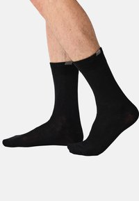 Sorte bomuldssokker med medium længde, der har en ensfarvet farve, ribbede manchetter og en subtil tekstur. Velegnede til daglig brug.
