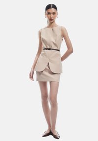 Robe sans manches beige avec un design cintré, taille ceinturée et bas évasé. Texture lisse et style minimaliste sans motifs.