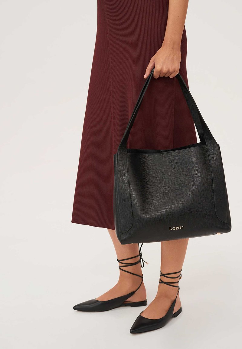 Fekete bőr bevásárlótáska texturált felülettel, két hosszú fogóval. Arany logó díszítés és elegáns, minimalista dizájn.