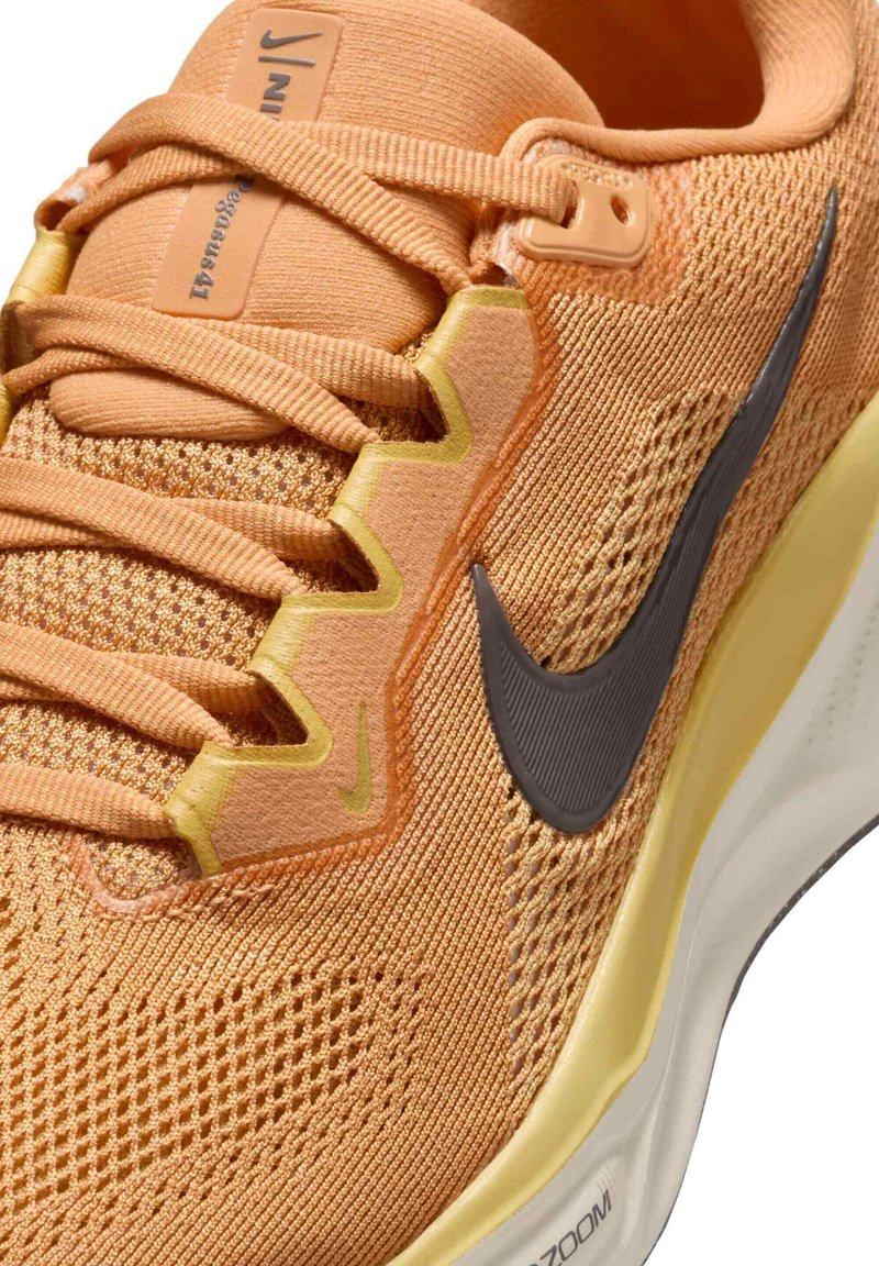 Zapatilla deportiva naranja con parte superior de malla texturizada, swoosh gris de Nike y suela acolchada con un acento amarillo. Sistema de cordones detallado.