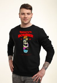 Svart sweatshirt med en färgglad grafik av ett skalle med blommor och en skateboard, med texten "STREET BOMBER 1990" i fet röd.