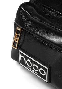 Borsa in similpelle nera con zip dorata, logo del marchio in rilievo bianco su un patch nero e superficie texturizzata.