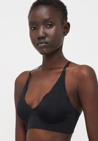 Black wireless bralette with a scalloped edge, made of smooth fabric. Features thin adjustable straps and a simple triangular design.