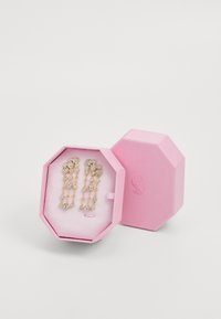 Gold-tone earrings with clear crystal embellishments displayed in a pink octagonal box with textured surface and white interior lining.
