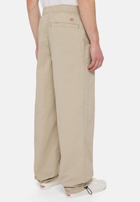 Beige cargo pants feature an elastic waistband, wide legs, and side pockets. The fabric appears lightweight with a smooth texture.