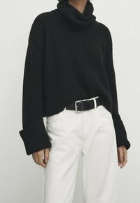 Black ribbed turtleneck sweater with wide sleeves, paired with white high-waisted pants and a black belt. Textured knit fabric.