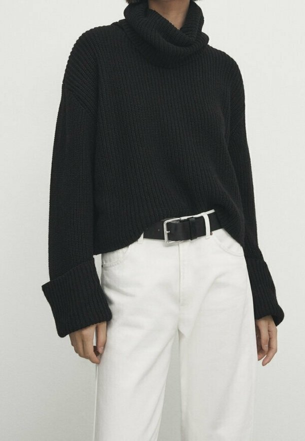 Black ribbed turtleneck sweater with wide sleeves, paired with white high-waisted pants and a black belt. Textured knit fabric.
