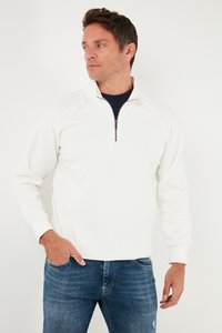 Kerge valge tõmblukuga pluus kõrge kaelusega ja raginaplastikuga varrukatega, kombineeritud siniste teksadega. Üksikasjalik logo on peenelt allääres.