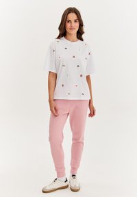 Biela bavlnená tričko s vyšívanými multicolor dizajnmi, kombinované s svetloružovými teplákmi. S uvoľneným strihom a okrúhlym výstrihom.