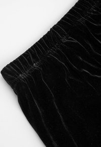 Czarna tkanina welwetowa z marszczoną talią, pokazująca gładką, miękką fakturę i delikatny połysk. Krawędź jest czysta i wykończona.