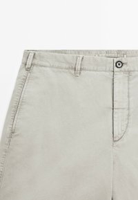 Beige Baumwoll-Chinos mit flacher Vorderseite, Knopfverschluss und zwei Seitentaschen. Verfügt über eine glatte Textur und Standardnaht.