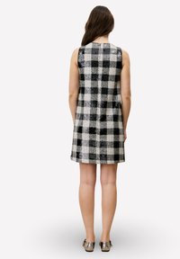 Robe sans manches à carreaux noirs et blancs avec une surface texturée, présentant une coupe droite et une fermeture éclair au dos.