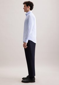 Camicia azzurro chiaro con maniche lunghe, abbinata a pantaloni navy scuri e scarpe eleganti nere, in vista laterale.