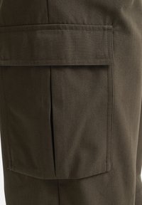 Pantalons cargo vert foncé en tissu texturé, avec une grande poche sur le côté et des détails cousus le long des coutures.