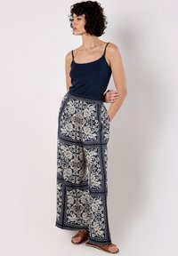 Marineblaue Spaghettiträgerbluse kombiniert mit weiter geschnittenen Hosen, die ein weißes Blumen- und geometrisches Muster aufweisen, mit elastischem Bund und hellbraunen Sandalen.