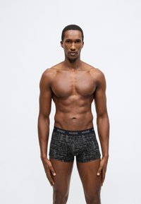 Μαύρα ανδρικά εσώρουχα μποξέρ με επαναλαμβανόμενο μοτίβο λογότυπου σε διαφορετικές αποχρώσεις του γκρι, με μαύρη ελαστική ζώνη μέσης που φέρει την ετικέτα "HUGO".