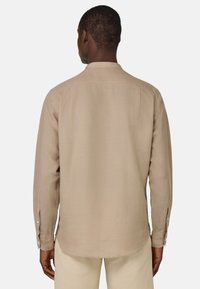 Camisa de manga larga en tejido beige claro. Presenta un cuello alto, puños con botones y un dobladillo recto con una textura suave.