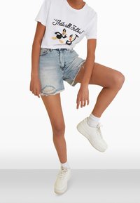 Camiseta blanca con un gráfico de dibujos animados, combinada con shorts de mezclilla desgastados de color azul claro y zapatillas blancas con una suela texturizada.