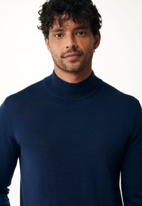 Suéter de cuello alto azul marino hecho de un material suave y de punto fino, con mangas largas y un diseño ajustado que incluye un alto cuello.