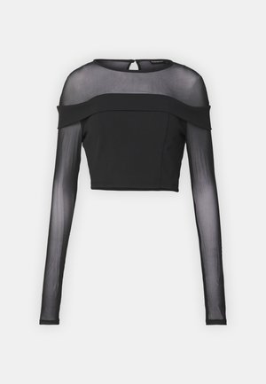 Fekete, rövidített felső hosszú áttetsző ujjal, egyszínű testtel, kerek nyakkivágással és váll nélküli kialakítással. Hátul kis hurokkal záródik.