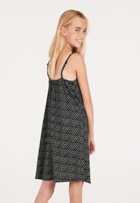 Robe noire avec une texture à motif, dotée de bretelles spaghetti réglables et d'une coupe ample. Le design arrive juste au-dessus du genou.