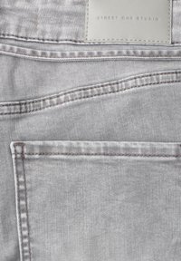 Tissu en denim gris clair avec surpiqûres doubles visibles et une étiquette blanche indiquant « STREET ONE STUDIO » près du bord supérieur.