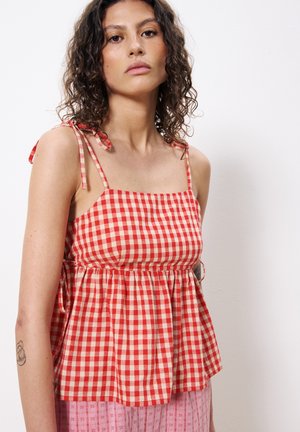 Crop top en vichy rouge et crème avec de fines bretelles, corsage ajusté et basque évasée. Fabriqué en tissu de coton léger.