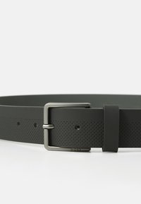 Ceinture en cuir noir avec boucle rectangulaire argentée mate et petits détails perforés le long de sa longueur sur fond blanc.