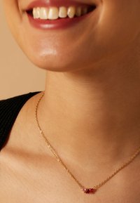 Gouden ketting met drie gekleurde edelstenen - twee rode en één roze - gezet in een delicaat, minimalistisch ontwerp dat mooi contrasteert met de huidtint.
