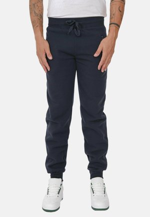 Pantaloni jogger navy in morbido tessuto con vita elastica e cordoncino, dotati di tasche laterali e polsini affusolati, abbinati a sneakers bianche.