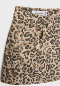 Jupe en denim imprimée léopard avec un fond beige et des taches noires, comprenant une poche avant et des accessoires métalliques à la taille.
