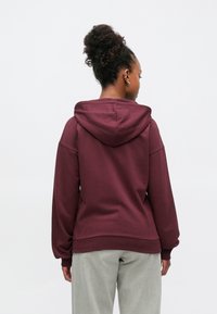 Sweat à capuche grenat avec cordon de serrage, manches longues et coupe décontractée. Le tissu a une texture douce et les poignets présentent des accents côtelés.