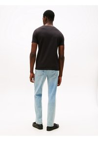 Czarny t-shirt z krótkim rękawem, o luźnym kroju, z okrągłym dekoltem. W zestawieniu z jasnoniebieskimi dżinsami i czarnymi butami. Prosty wzór, bez nadruków.