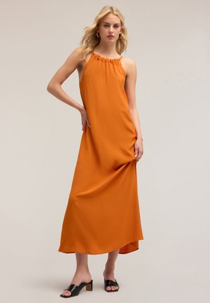 Vestido largo sin mangas de color naranja con escote fruncido, tela suave y corte holgado. Se lleva con unas mule negras de punta abierta, con tacón cuadrado.