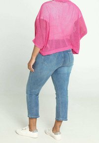 Rosa mesh oversized topp, blå skinny jeans och vita sneakers med silverdetaljer. Toppens design är löst sittande och öppen, luftig.