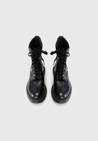 Bottines en cuir noir avec un bout rond, un laçage à l'avant et un col rembourré; présentent des œillets métalliques et une semelle en caoutchouc épaisse.