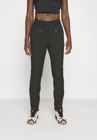 Pantalones ajustados verde oscuro con una textura suave, que presentan bolsillos frontales con cremallera y una cintura clásica, combinados con zapatillas blancas y naranjas.
