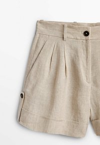 Shorts en lin beige avec plis, dotés d'une fermeture à bouton et d'un ourlet retroussé. Le tissu a une finition lisse et légèrement texturée.